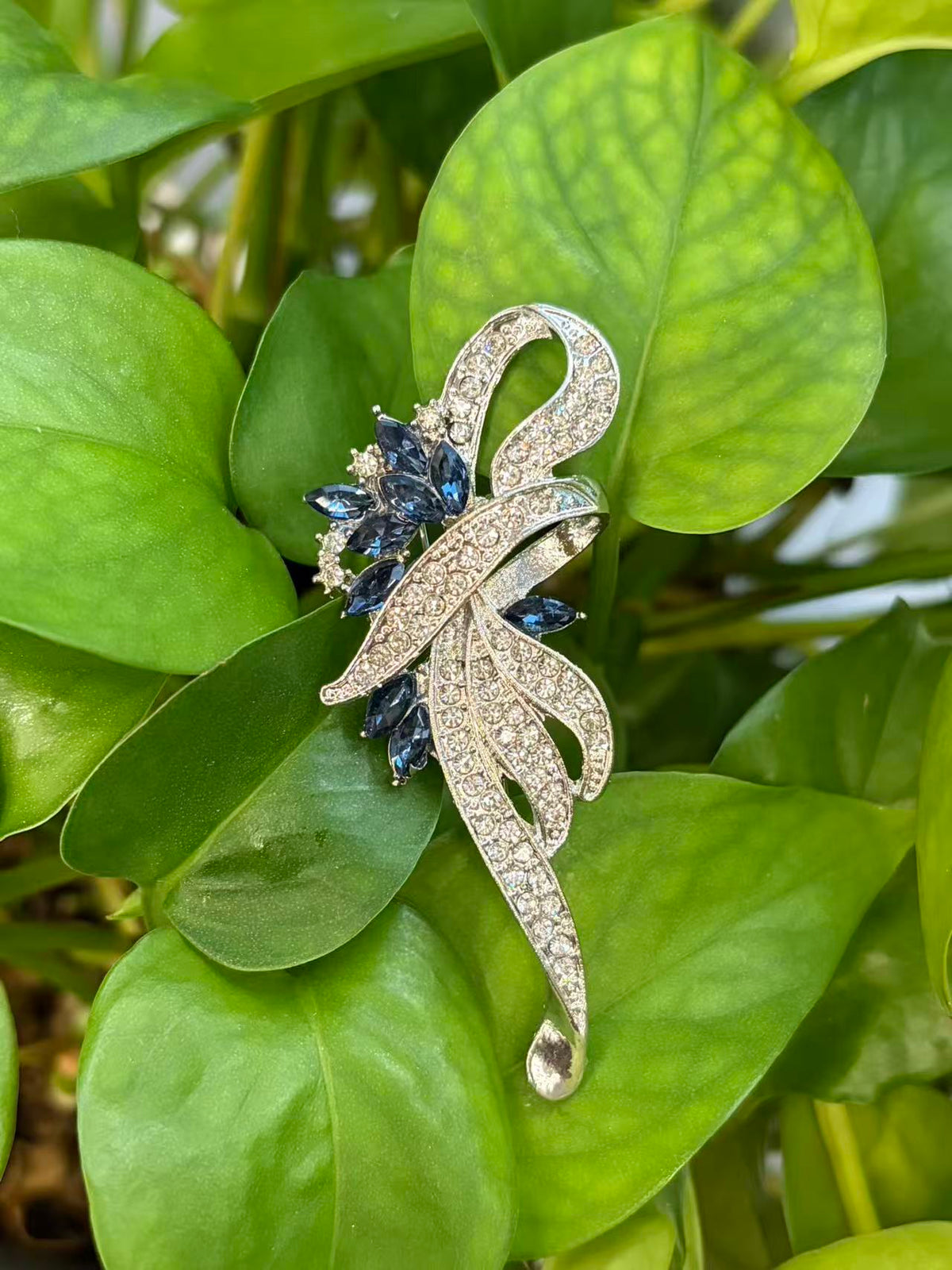 Crystal floral brooch pin displayed on green plant leaves