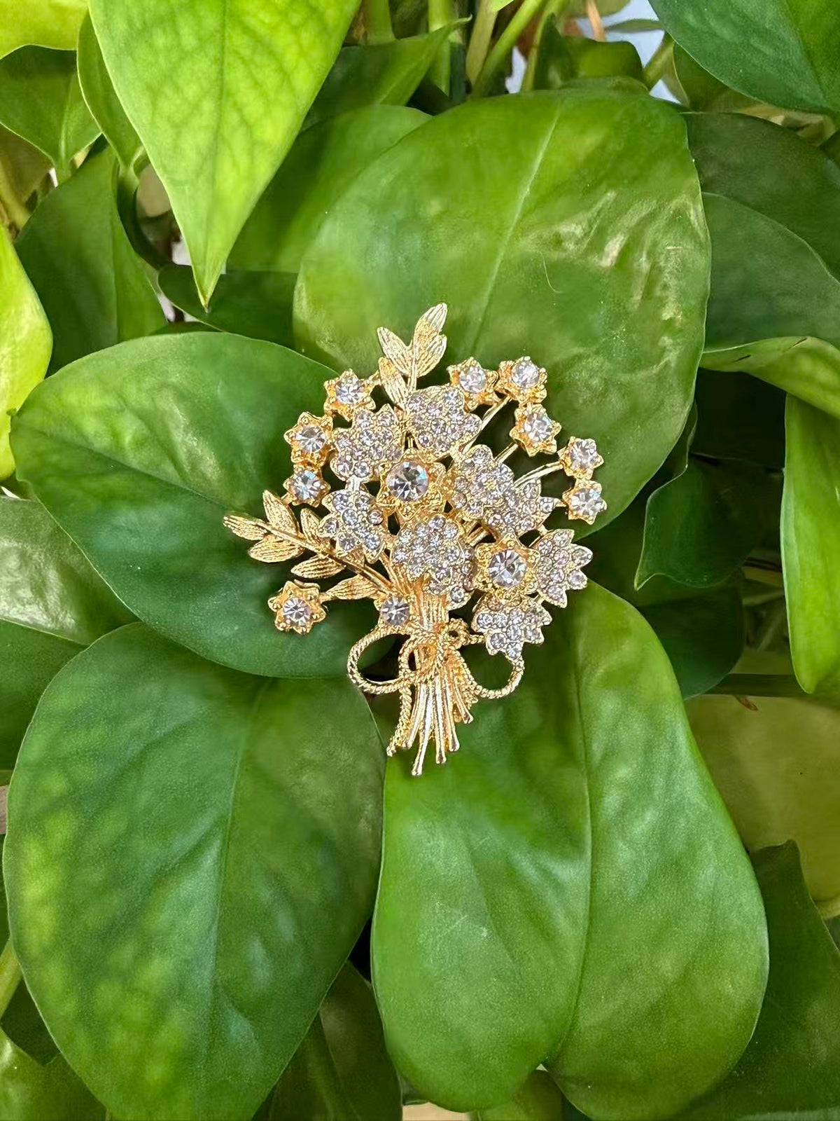 Crystal flower bouquet brooch pin displayed on green plant leaves