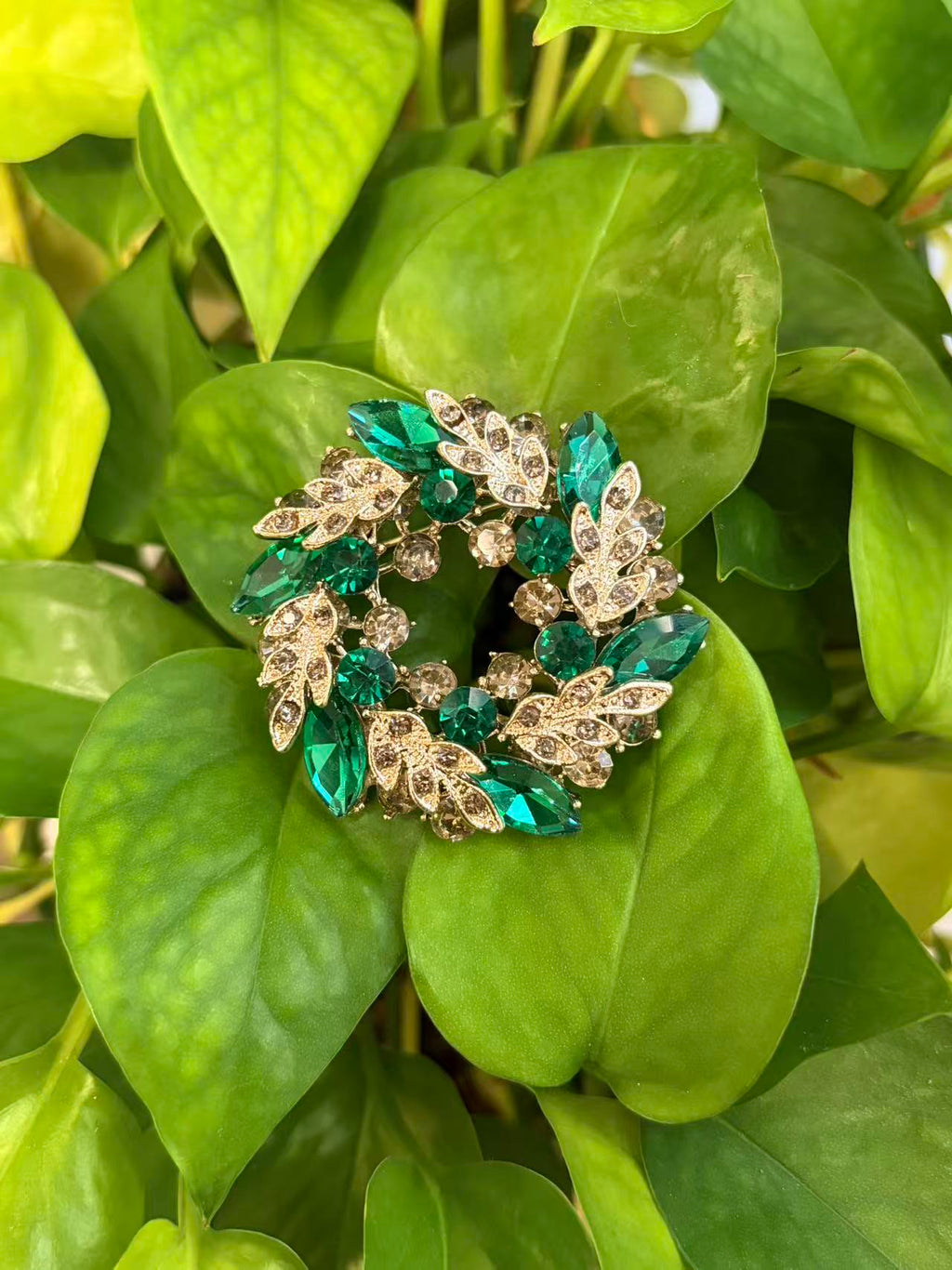 Crystal leaf wreath brooch pin displayed on green plant leaves