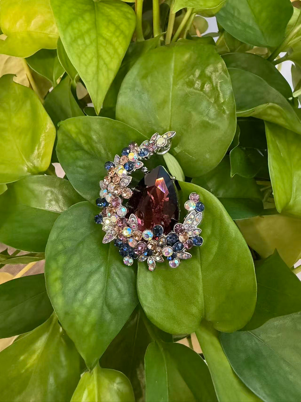 Crystal teardrop floral brooch pin displayed on green plant leaves